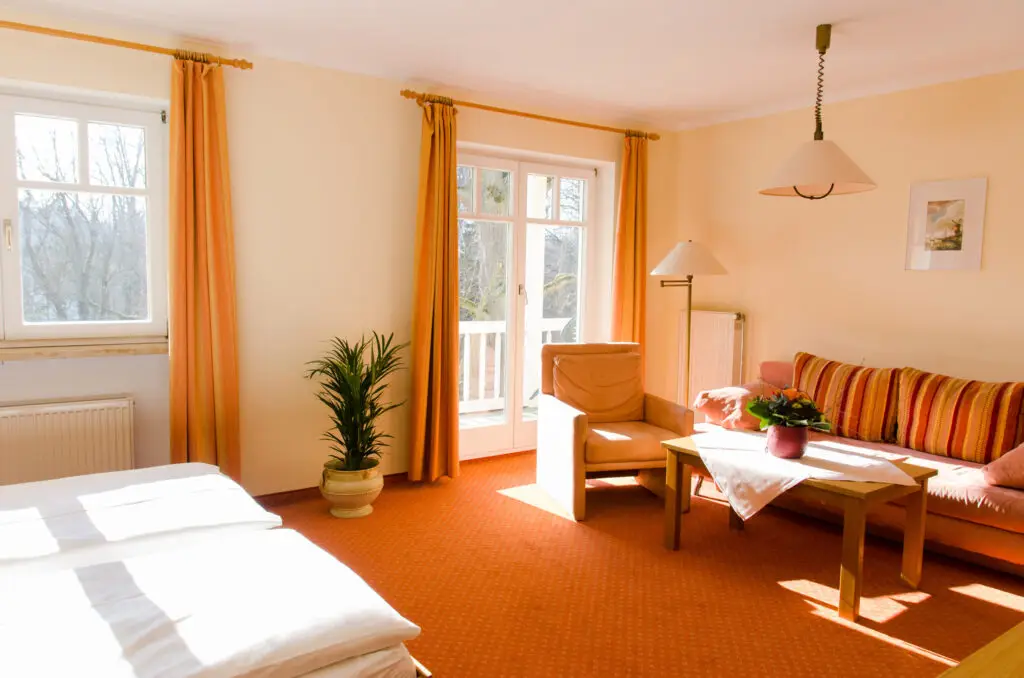Helles, geräumiges Zimmer mit Doppelbett, gemütlichem Sofa und orangen Vorhängen.
